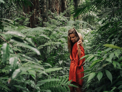 A woman in a captivating red dress gracefully wanders alone through the enchanting forests of Bali, Indonesia, immersed in the mystical beauty of her serene surroundings