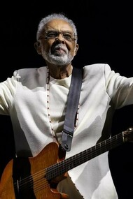 Gilberto Gil no palco, durante a turnê Tempo Rei, no Mineirão, em 2025, com os braços abertos, a guitarra presa ao corpo e um fundo completamente escuro. De braços abertos diante do público, o artista parece acolher as muitas histórias e gerações que sua música acompanhou ao longo de mais de seis décadas de carreira. Do primeiro LP Realce ouvido aos 10 anos ao show de despedida dos grandes palcos, sua música atravessou décadas e se misturou às memórias de uma vida. Sob a luz do palco, a imagem parece traduzir o próprio espírito da canção: o tempo passa, transforma as formas do viver e, ainda assim, algumas músicas permanecem