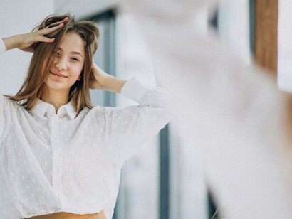 A confident young woman in a casual outfit looks at her reflection in the mirror