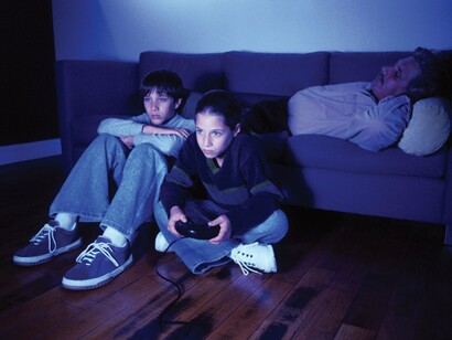 Dos niños juegan a la videoconsola mientras su padre duerme en el sofá
