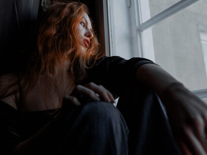 A young woman, burdened by depression and anxiety, sits contemplatively by the window, lost in her thoughts