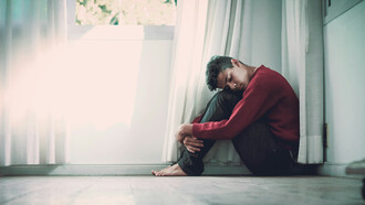 A barefoot young man hugging his legs, trying to sooth himself