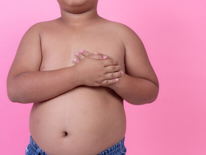 An overweight boy stands against a pink background, illustrating childhood obesity