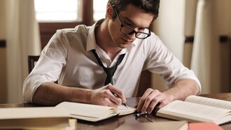 Un hombre escribe en un cuaderno sobre su escritorio
