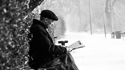 Velhinho sentado na praça lendo jornal no inverno