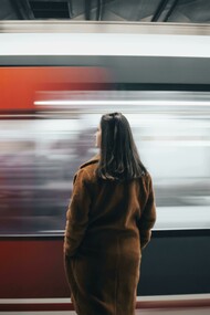 Woman in a brown coat standing alone as a speeding train passes by
