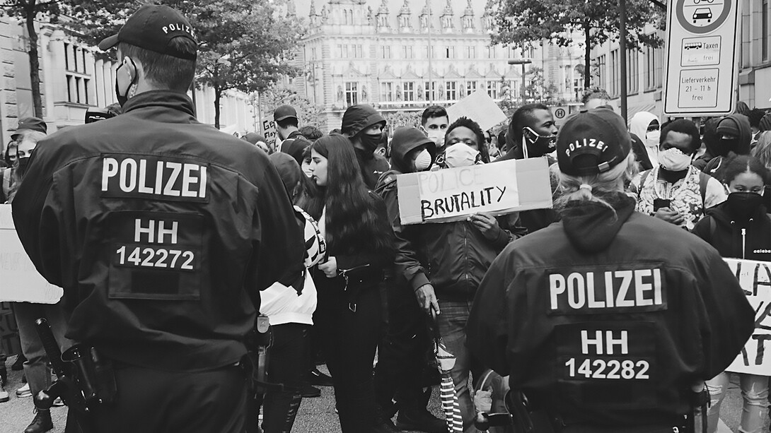 Protesters holding signs that read 'Police Brutality' stand defiantly in front of a line of police officers