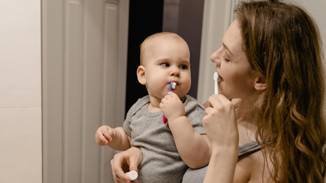 Mãe com bebê de colo escovam os dentes juntas