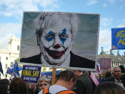 A person holding an image of Boris Johnson with clown face art, resembling the Joker