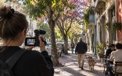 A woman capturing an ordinary city scene on camera, reflecting Tiranos Temblad’s fascination with the unexpected moments hiding in plain sight