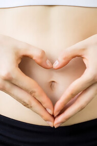 Close-up of female hands forming a heart shape on her belly, symbolizing improved gut health and well-being