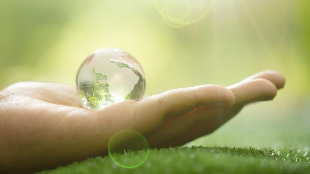 A human hand cradling a transparent globe, highlighting the interconnectedness of humanity and Earth's resources