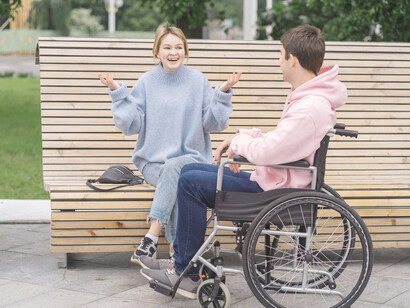 A couple sitting in the park having a conversation, the man in a wheelchair speaking with a woman