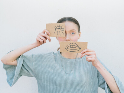 A woman covers her eye and mouth with a cardboard eye and mouth