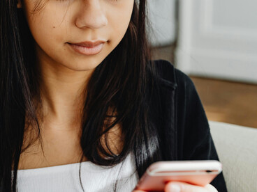 A woman in a black long-sleeved top uses her mobile phone while binge-watching a vertical series made up of short smartphone drama episodes