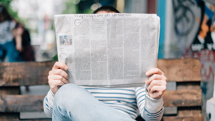 A man sitting on a bench, reading a newspaper 