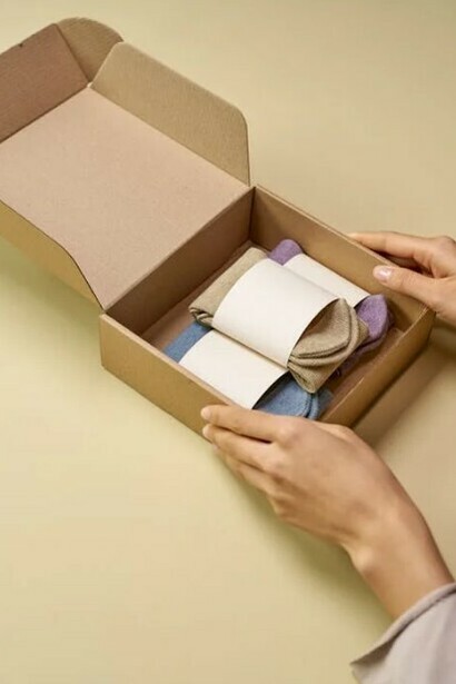 A person carefully preparing a cardboard box filled with garments made from biodegradable fibers, supporting the movement toward sustainable fashion