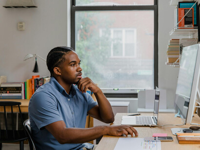 A man is seated at his desk in a home office, speaking on the phone