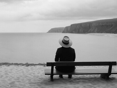 A person sitting on a bench by the shore, reflecting
