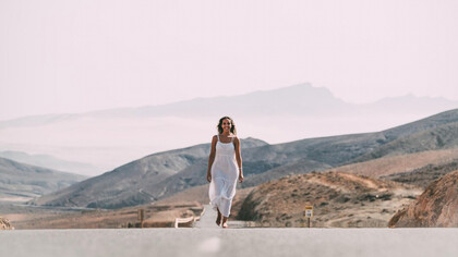A woman walking on a road near hills under a cloudy sky, smiling, symbolizing her healing journey, spiritual warfare, and overcoming trauma, embodying peace and purpose