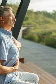 An older man resting one hand on his chest and the other on his abdomen as he breathes deeply, symbolizing awareness of the body's natural rhythm
