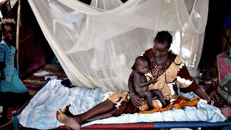 A Nilote woman laying with her baby son and her little daughter standing close by the bed, Africa