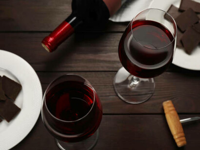 A tasteful pairing of red wine glasses and chocolate truffles on a warm wooden surface