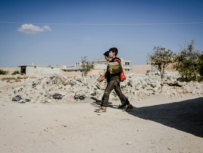 Students walking along an unpaved road in a war-torn city among ruins, Idlib, Idlib Governorate, Syria