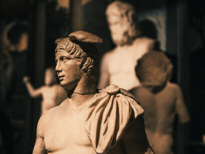Escultura griega de un hombre con túnica, expuesta junto a otras piezas arqueológicas