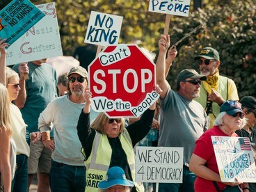 Demonstrators gathering with messages defending democracy and collective action, reflecting the public pushback against authoritarian ideas and political overreach