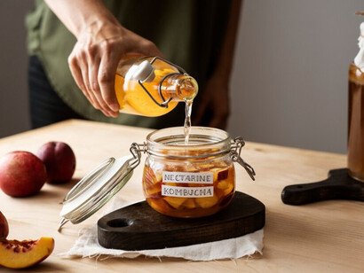 A woman preparing a jar of nectarine kombucha with a label on it