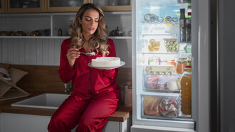 A woman eating at night in front of an open fridge, suggesting binge eating