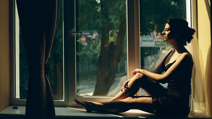A woman sitting quietly by a sunlit window, representing the emotional patterns carried from childhood into adulthood