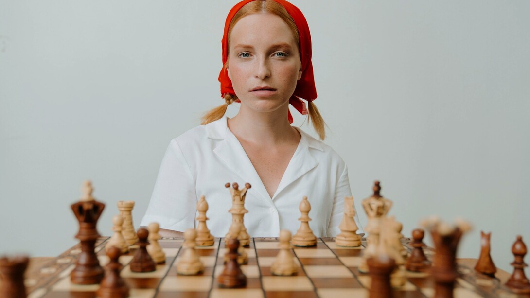 Mulher de camisa branca joga xadrez no tabuleiro de madeira marrom