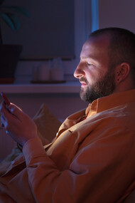 In the dim glow of his phone, a man searches for connection, but the quiet room around him reflects the hollowness of digital intimacy