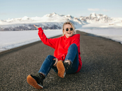 In Iceland, a stylish woman poses on an empty road as a lone traveler walks away into the distance