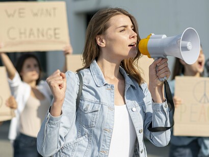 A young woman uses a megaphone to amplify her voice during a protest, symbolizing the power of collective action and the crucial role of political participation in advocating for rights and policy changes