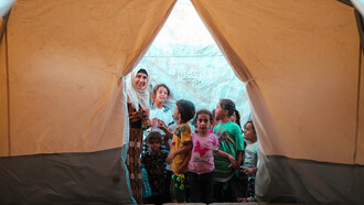 Displaced by conflict in the Middle East, a group of refugees gathers inside a tent
