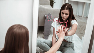 A teenage girl looks at the word ugly in a mirror