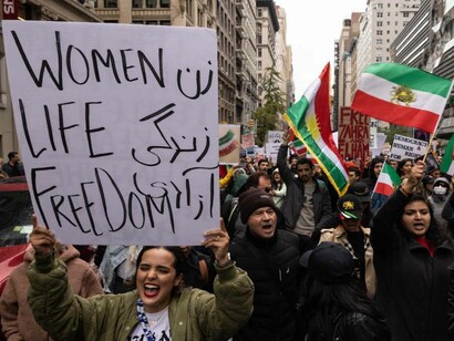 A woman holding up a sign reading "women, life, freedom" and marching in protest again the Iranian government in Iran