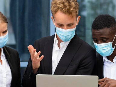 Professionals working during the COVID-19 pandemic, wearing masks and using laptops, showcasing the adaptation to remote work environments and health safety measures