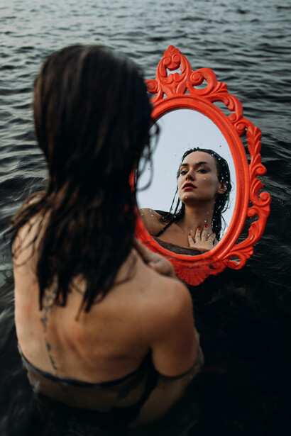 A woman in a bathing suit looking at her reflection in the sea
