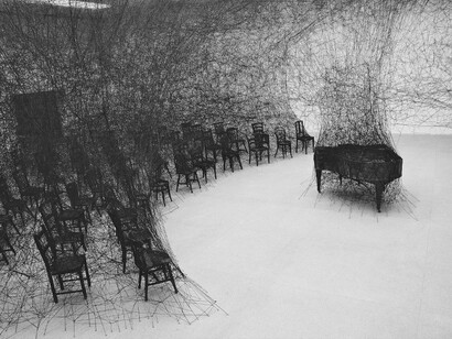 Chiharu Shiota. Instalación titulada "En silencio", 2008. La obra consiste en un piano de cola quemado rodeado de sillas quemadas, todo ello entrelazado con millas de hilo de lana negra
