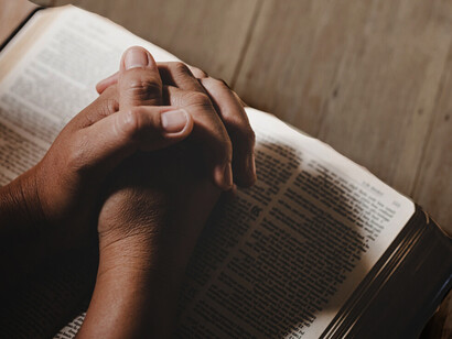 Hands gently clasped in prayer over a Bible in a peaceful church setting, symbolizing spirituality and trust in God