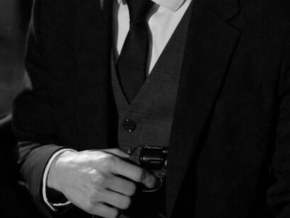 A sharply dressed man grips a small pistol with an intense gaze, embodying the glorified portrayal of criminals in true crime media