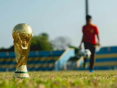 A gold trophy placed on the grass field under the bright daylight, with a football positioned beside it