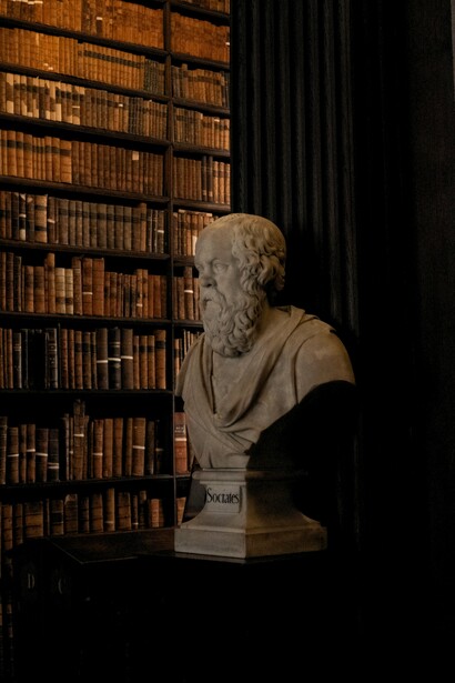 A bust of Socrates standing among rows of books, representing the historical relationship between knowledge, literature, and intellectual thought
