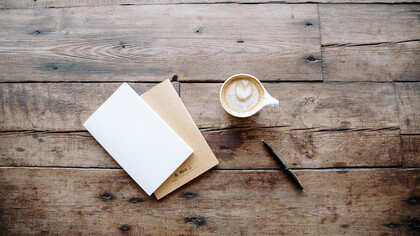 Dos libretas, una tasa de café y un bolígrafo encima de una mesa de madera
