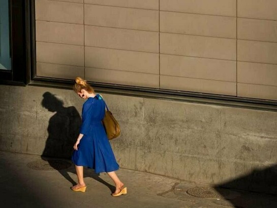 Uma mulher caminha sob a luz do fim do dia, acompanhada pela própria sombra. Entre aquilo que se revela e aquilo que permanece oculto, a felicidade também pode carregar suas contradições