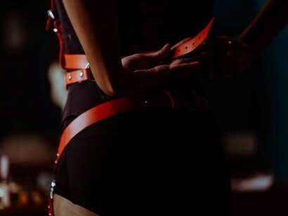 A woman in a bedroom wearing a red sexy belt and black lingerie, highlighting themes of gender stereotypes, erotic expression, and objectification